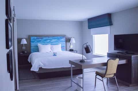 Modern hotel room with king bed, blue headboard art, work desk, flat-screen TV, and contemporary decor