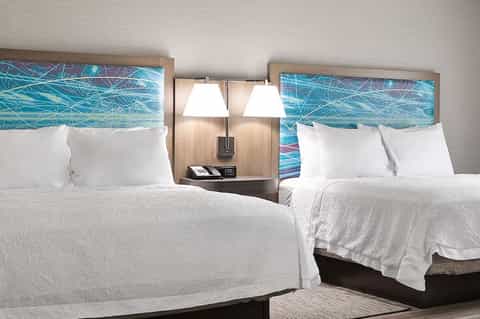 Hotel guest room with two queen beds, blue headboard artwork, bedside lamps, and modern furnishings