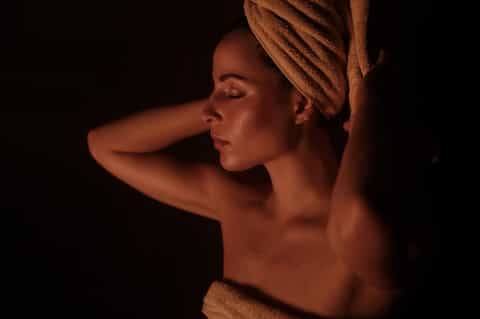 Woman with towel wrapped around head in warm studio lighting against dark background