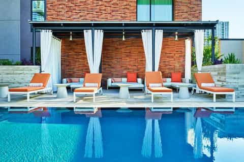 Luxury poolside lounge area with white curtained cabanas, orange loungers, and modern pergola structure by blue swimming pool