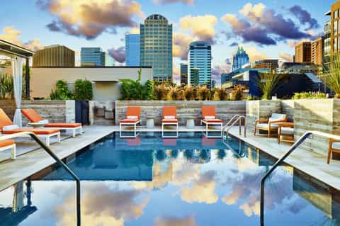 Luxury rooftop pool with orange loungers, modern amenities, and downtown city skyline backdrop