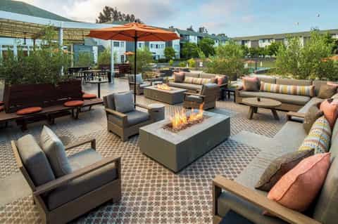 Expansive outdoor patio with fire pit, lounge seating, striped cushions, orange umbrella, and geometric patterned flooring