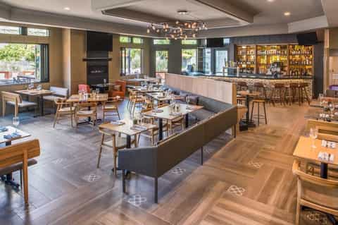 Modern restaurant and bar interior with wooden furniture, fireplace, and well-stocked liquor shelves