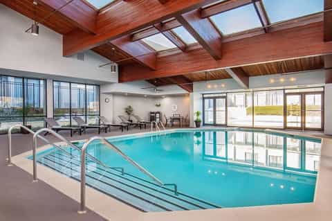 Indoor hotel pool with turquoise water, wooden beam ceiling, skylights, and seating area views