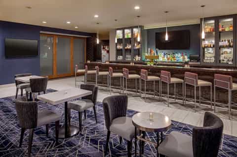 Modern hotel bar lounge with navy walls, upholstered seating, and bar counter with pendant lighting