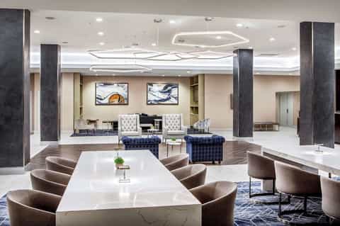 Modern hotel lobby with white marble table, contemporary seating, dark columns, and artistic ceiling lighting