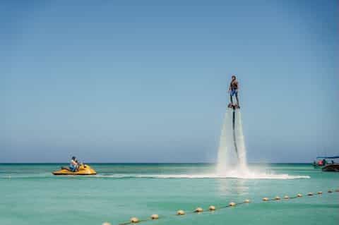 Man performing flyboarding over turquoise ocean water with jet ski support