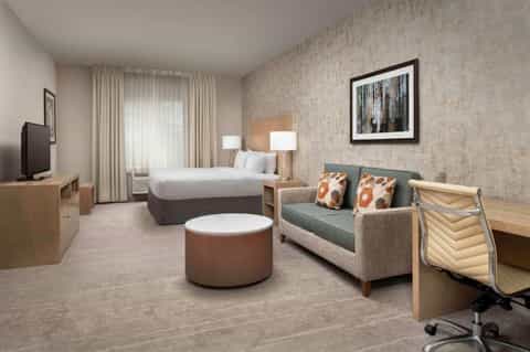 Spacious hotel suite with king bed, seating area, desk, and patio access