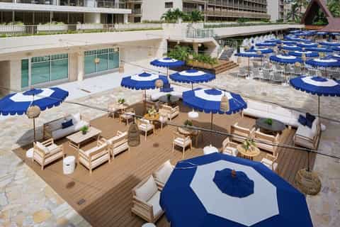 Elevated view of resort deck with wooden lounge areas, blue umbrellas, and blue-and-white umbrellas over seating