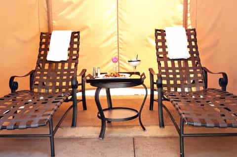 Luxury glamping tent interior with two striped loungers facing a small table with refreshments