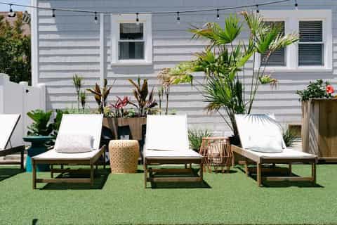 Rooftop lounge with wooden loungers, tropical plants, and string lights on green turf