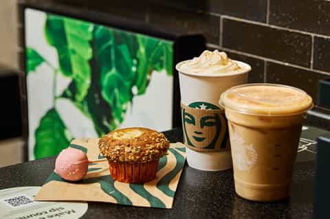 Starbucks beverages and pastries displayed on dark counter with menu screen behind
