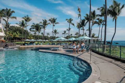 Curved resort pool with infinity edge, lounging guests, umbrellas, and ocean horizon