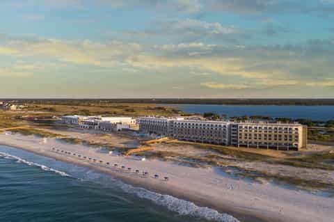 Beachfront resort aerial view showing buildings along sandy shore and bay landscape