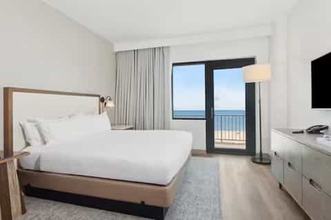 Modern hotel bedroom with ocean-view balcony, queen bed, and contemporary furnishings