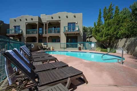Resort pool with turquoise water, lounge chairs, and Pueblo-style building