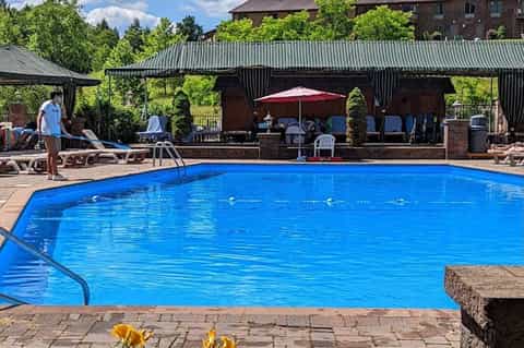 Resort swimming pool with blue water, covered cabana area, lounge chairs, and brick building backdrop