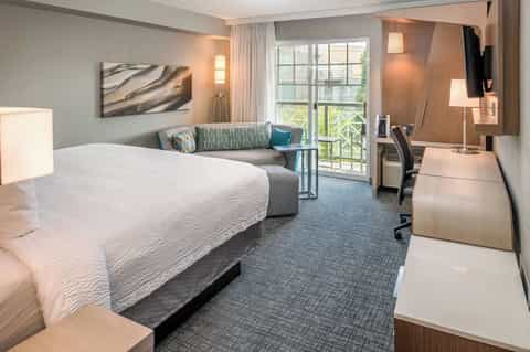 Spacious hotel room with king bed, comfortable seating area, balcony doors, and modern décor