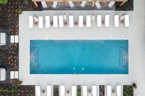 Overhead view of rectangular pool surrounded by white lounge chairs and umbrellas on light stone deck