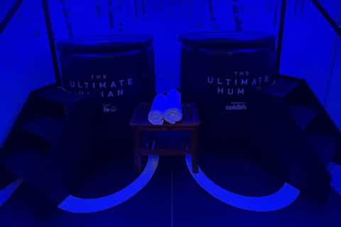 Illuminated spa pods labeled 'The Ultimate Human' with blue neon glow and footwear display