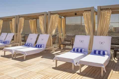 Luxurious poolside cabanas with white lounge chairs, cream curtains, and gold pergolas