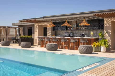 Modern pool bar and lounge area with teak accents, woven seating, and palm plants