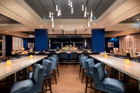 Modern hotel bar lounge with blue accent walls, marble counters, pendant lighting, and seating