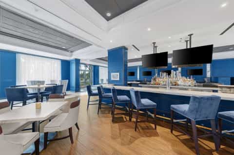 Contemporary hotel club room with blue walls, white furnishings, bar, and floor-to-ceiling windows