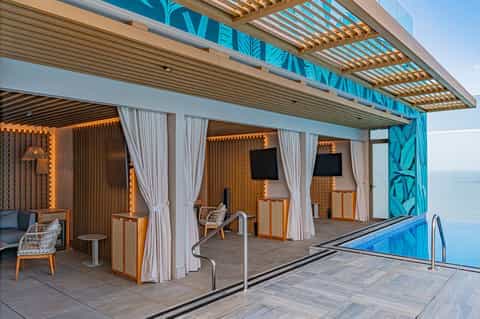 Poolside lounge area with wooden pergola, white curtains, and ocean views