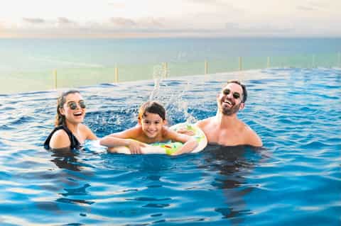 Family enjoying rooftop pool with ocean backdrop and clear blue water