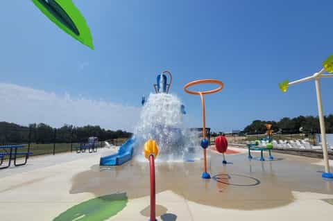 Splash pad water play area with bucket pour feature, water jets, and colorful interactive elements