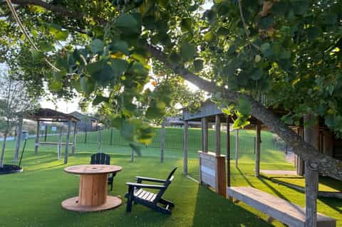 Outdoor seating area with fire pit table, Adirondack chairs, wooden pergolas, and mature trees on green lawn