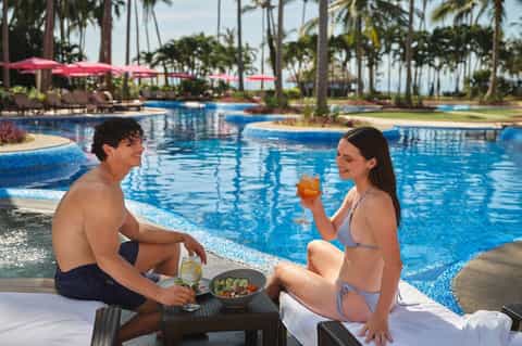 Couple relaxing poolside with tropical umbrellas and ocean backdrop