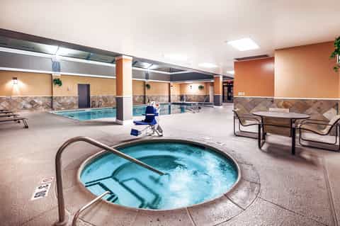 Indoor pool complex with hot tub in foreground, orange and tan walls, multiple seating areas, and columns