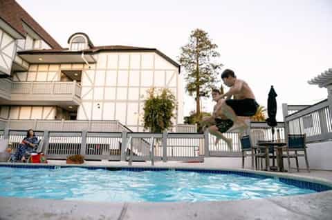 Resort pool with guests jumping in, Tudor-style building with white railings in background