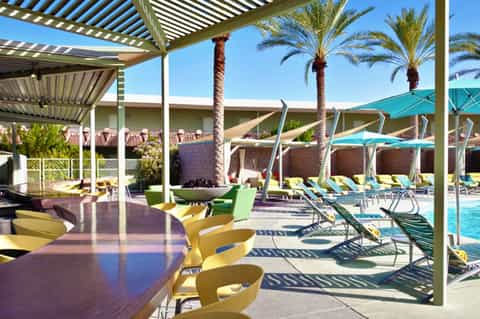 Modern pool area with pergolas, colorful lounge chairs, umbrellas, and palm trees under clear sky