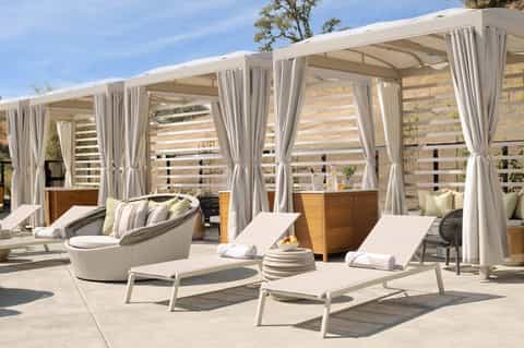Luxurious resort terrace with lounge chairs, curved seating, pergolas with white curtains, and stone accent wall