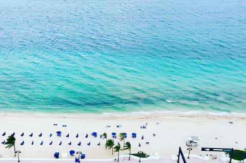 Aerial view of pristine beach with blue umbrellas, white sand, and turquoise ocean water