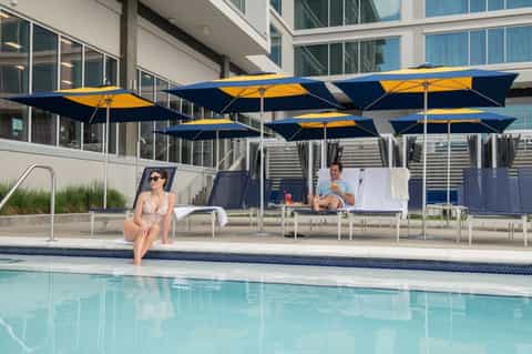 Resort pool with blue and yellow umbrellas, lounge chairs, and modern building facade on sunny day