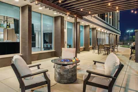 Elegant outdoor patio with firepit, lounge chairs, dining area, brick columns, and nighttime ambient lighting