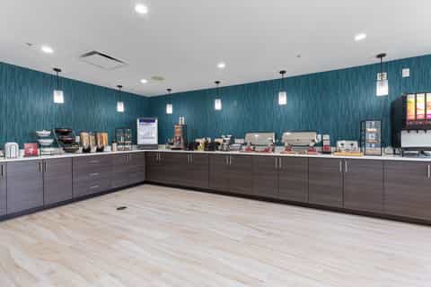 Modern coffee bar with teal accent wall, espresso machines, pastry display, and beverage service counter