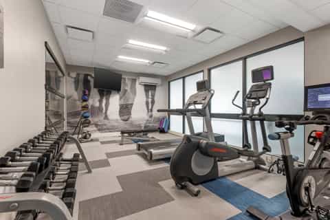Modern fitness center with cardio equipment, treadmill, stationary bikes, dumbbells, and wall-mounted TV