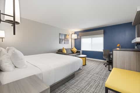 Spacious hotel room featuring queen bed, blue wall, yellow chair, and seating area