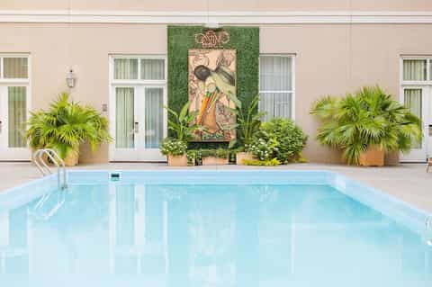 Indoor heated pool with artistic wall mural, tropical plants, and cream-colored building facade