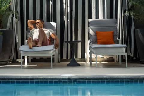 Guest relaxing on poolside lounge chair with striped privacy screens and pool view