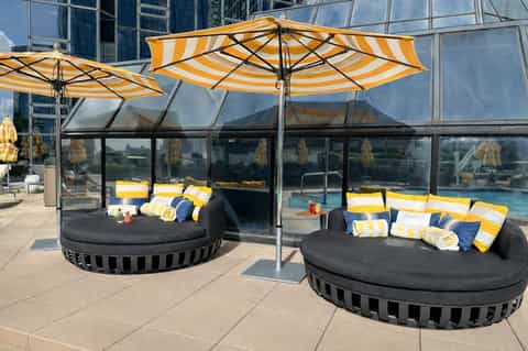 Outdoor pool deck with round sunbeds under yellow-striped umbrellas and contemporary lounge seating