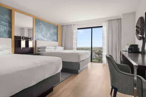 Modern hotel room with two queen beds, ocean view balcony, wooden accents, and contemporary furnishings