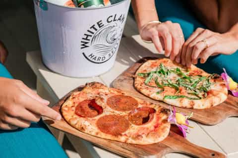White Claw hard seltzer bucket with gourmet pizzas on wooden serving boards