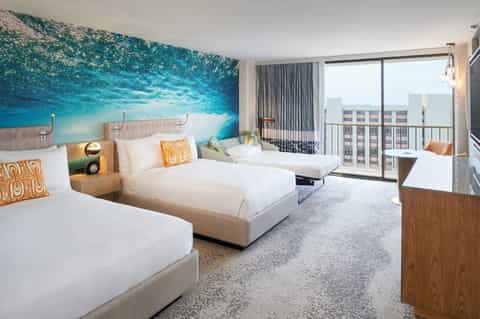 Beachfront hotel room with two beds, ocean mural headboard, and ocean view balcony