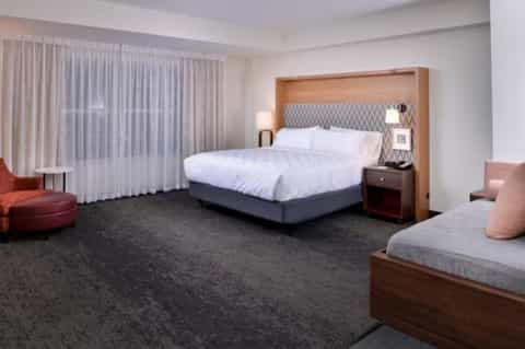 Spacious hotel suite with queen bed, sofa, wood furniture, curtained windows, and modern decor